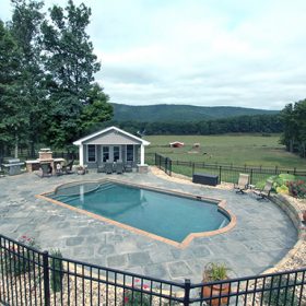 Wrought iron fence around Grecian pool with flagstone deck and pool house. Diamond Brite French Gray exposed aggregate pool finish installed by National Pools of Roanoke
