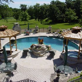 Freeform pool overlooking golf course with spas in tiki huts and waterfalls. Features Diamond Brite exposed aggregate pool finish installed by Barrington Pools.