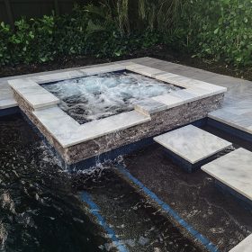 Up close photo of Pool and spa in backyard with River Rok Emerald Black natural pebble finish with marble decking. Installed by Tropical Oasis Pool & Spa.