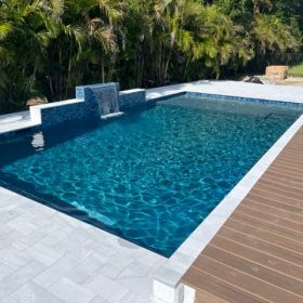 Pool with Bahama Breeze finish with waterfall, white stone pavers and teak deck.