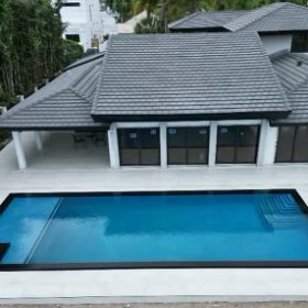 A drone shot of a rectangular pool finished with Tanzanite, with black coping on a white stone deck.