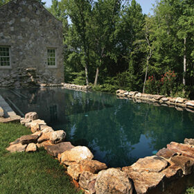 Sunny photo of a rectangular pool attached to an old fieldstone building.