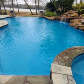Large backyard pool area with spa, water features, sun shelf and large patio with furniture and brick fireplace.