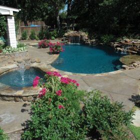 Freeform pool and spa with natural stone water features and floral landscaping around the pool area.